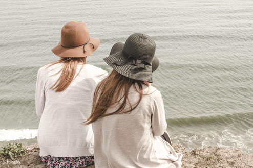 Deux femmes portant des chapeaux assises au bord de l’eau