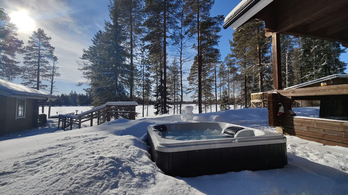 Bain à remous sur la terrasse enneigée près de la maison en bois
