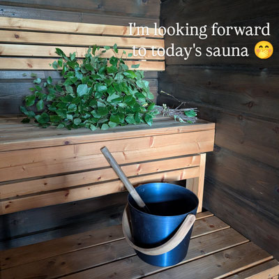 Branches de bouleau et seau de sauna devant un mur en bois