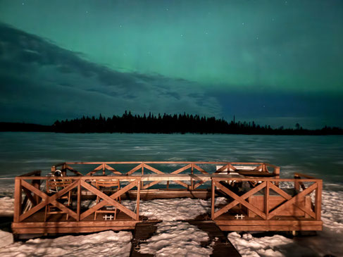 Aurora boreal sobre el lago más allá de una barandilla de madera