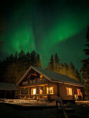 Grüne Nordlichter über einem beleuchteten Holzhaus