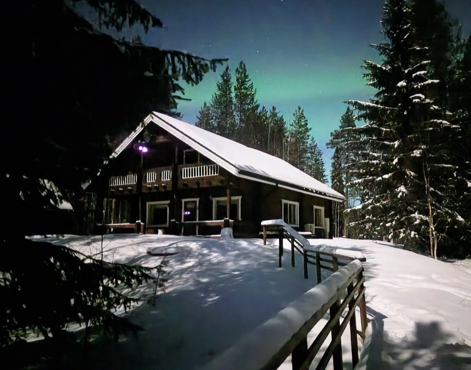 Grüne Nordlichter über dem verschneiten Hauptgebäude von Mökki Tikka